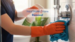Person cleaning a chrome shower fixture in an American-style bathroom with gloves and spray, focusing on hard water stain removal.