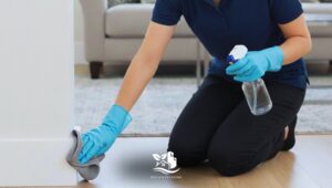 Woman cleaning baseboards and molding in a bright and tidy American-style living room to prepare the home for the holidays.